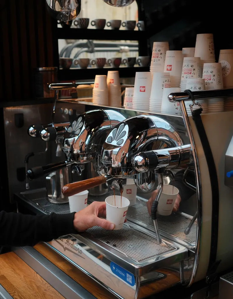 Barista laver espresso på en professionel espressomaskine med illy-kopper stablet ovenover