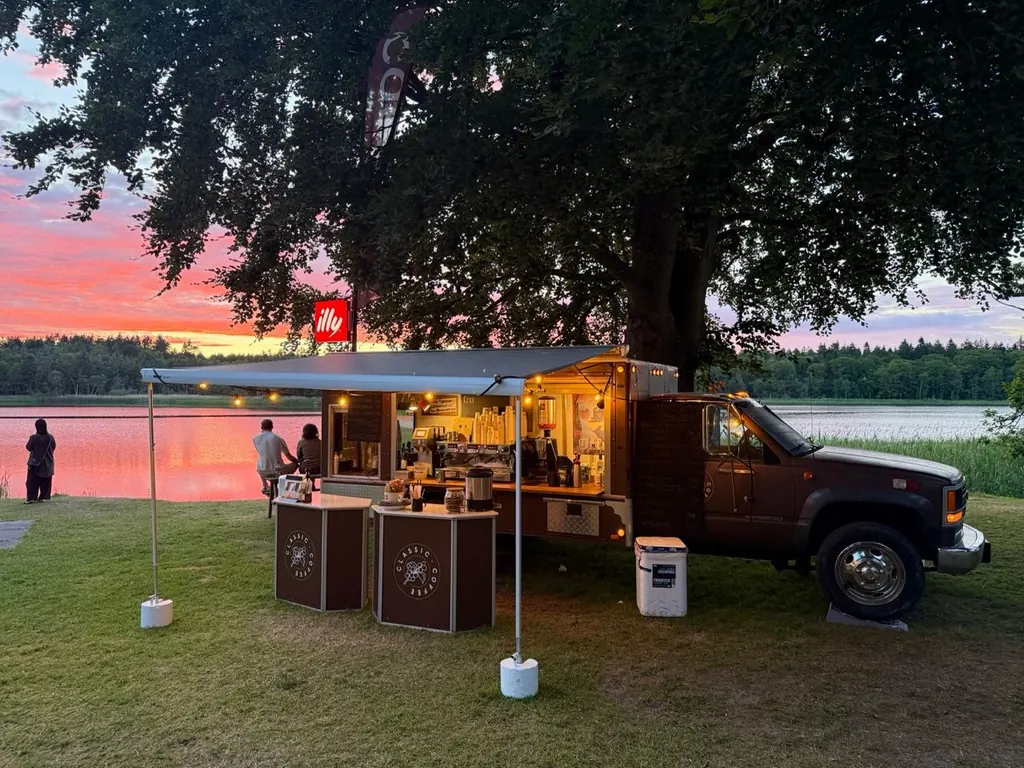 Classic Coffee-kaffebil med illy-skilt og lysguirlander ved en sø i solnedgang