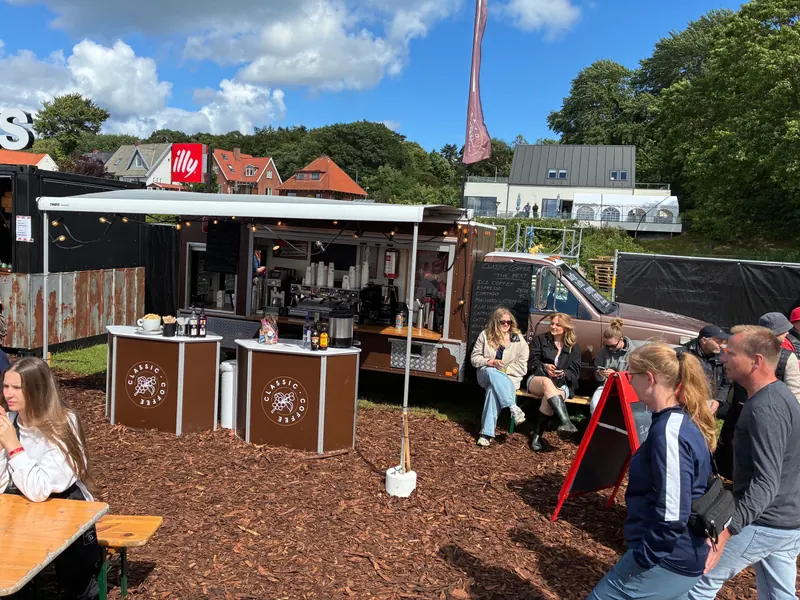 Kaffebilen King til et udendørs event, hvor gæster sidder ved træborde